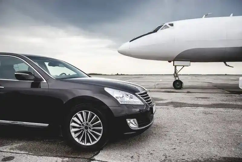 The front of a black luxury sedan is parked on an airport tarmac, with a private jet in the background, symbolizing premium IAH to Galveston transfer service.